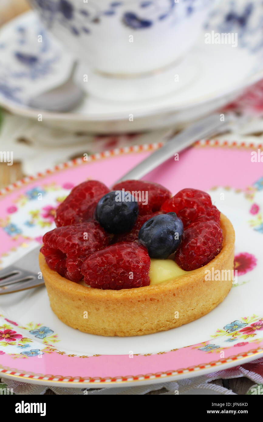 Köstliche Tartelette mit Vanillesauce, frische Himbeeren und Blaubeeren auf rosa Teller Stockfoto