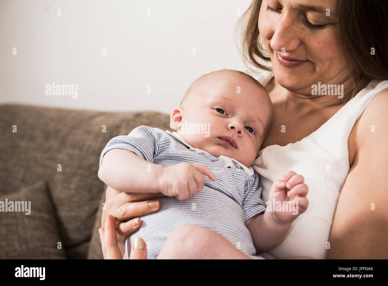 Lächelnde Mutter ihren kleinen Sohn auf dem Sofa sitzend hält Stockfoto