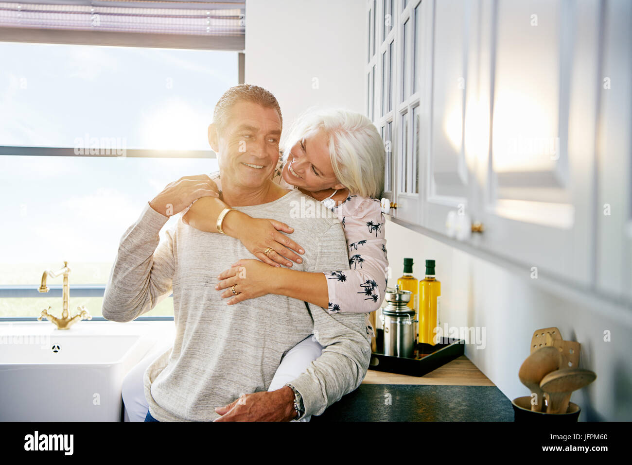 Inhalt älteres paar lächelnd und gemeinsam einen liebevollen Moment zusammen und entspannen Sie in ihrer Küche zu Hause Stockfoto