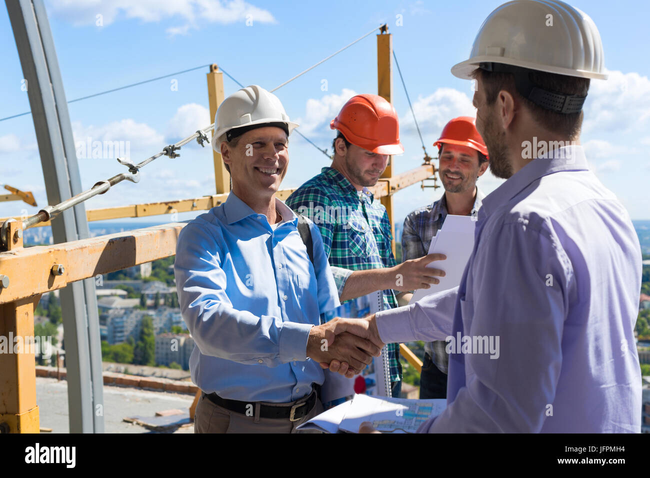 Bauherren-Handshake, zwei glücklich lächelnde Partner, die Hand zu schütteln, nach einem Treffen mit Vorarbeiter Team vor Ort Stockfoto
