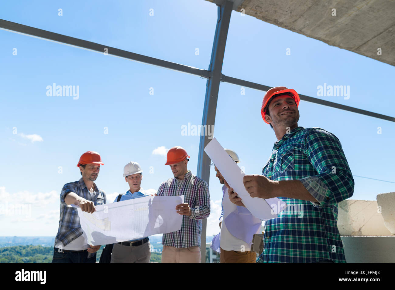 Gruppe von Bauherren In Bauarbeiterhelm halten planen Projekt bauseits Constuction Bauingenieure gemeinsam diskutieren Stockfoto