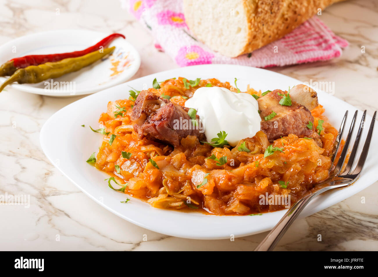 Kohl-Eintopf mit geräuchertem Schweinefleisch Rippen, Creme und grün Petersilie serviert in weißen Teller mit eingelegtem Chili Paprika und Brot Stockfoto