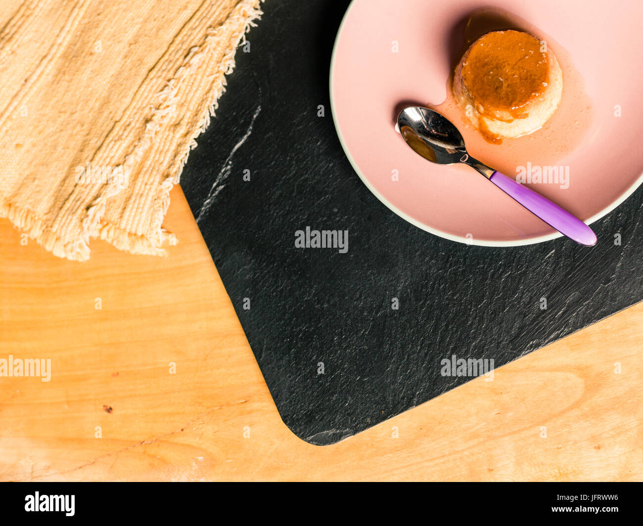 Flan oder Creme Karamell Pudding ist ein Pudding mit einer Schicht aus weichem Karamell auf der Oberseite, Herkunft sind französisch und spanisch mit Löffel über Holztisch Stockfoto