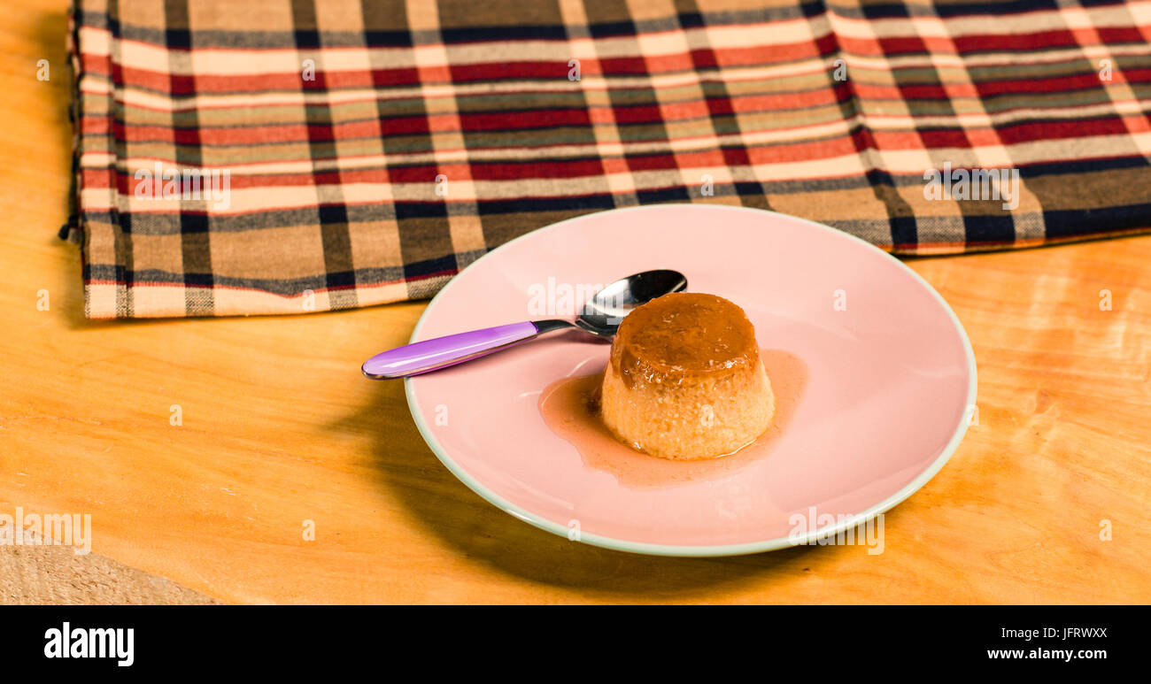 Flan oder Creme Karamell Pudding ist ein Pudding mit einer Schicht aus weichem Karamell auf der Oberseite, Herkunft sind französisch und spanisch mit Löffel über Holztisch Stockfoto