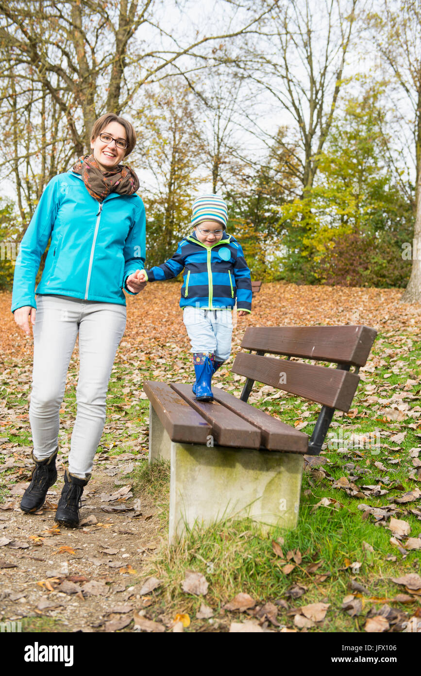 Mutter, die an Hand des Sohnes zu Fuß auf der Parkbank im Herbst Stockfoto