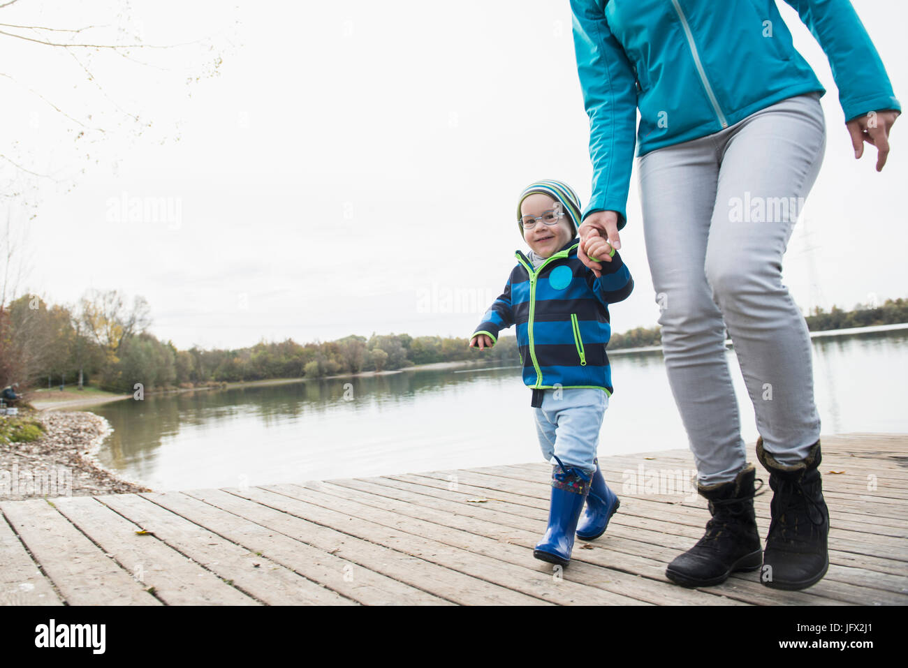 Mutter und Sohn gehen hand in Hand auf einem Bootssteg über See im Herbst Stockfoto