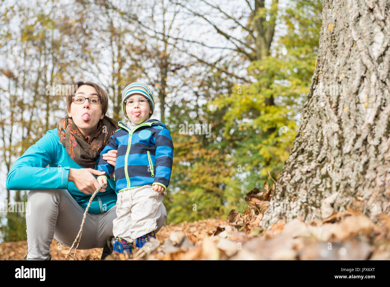 Porträt von Mutter und Sohn herausragen Zunge Big Baumstamm im Herbst Stockfoto