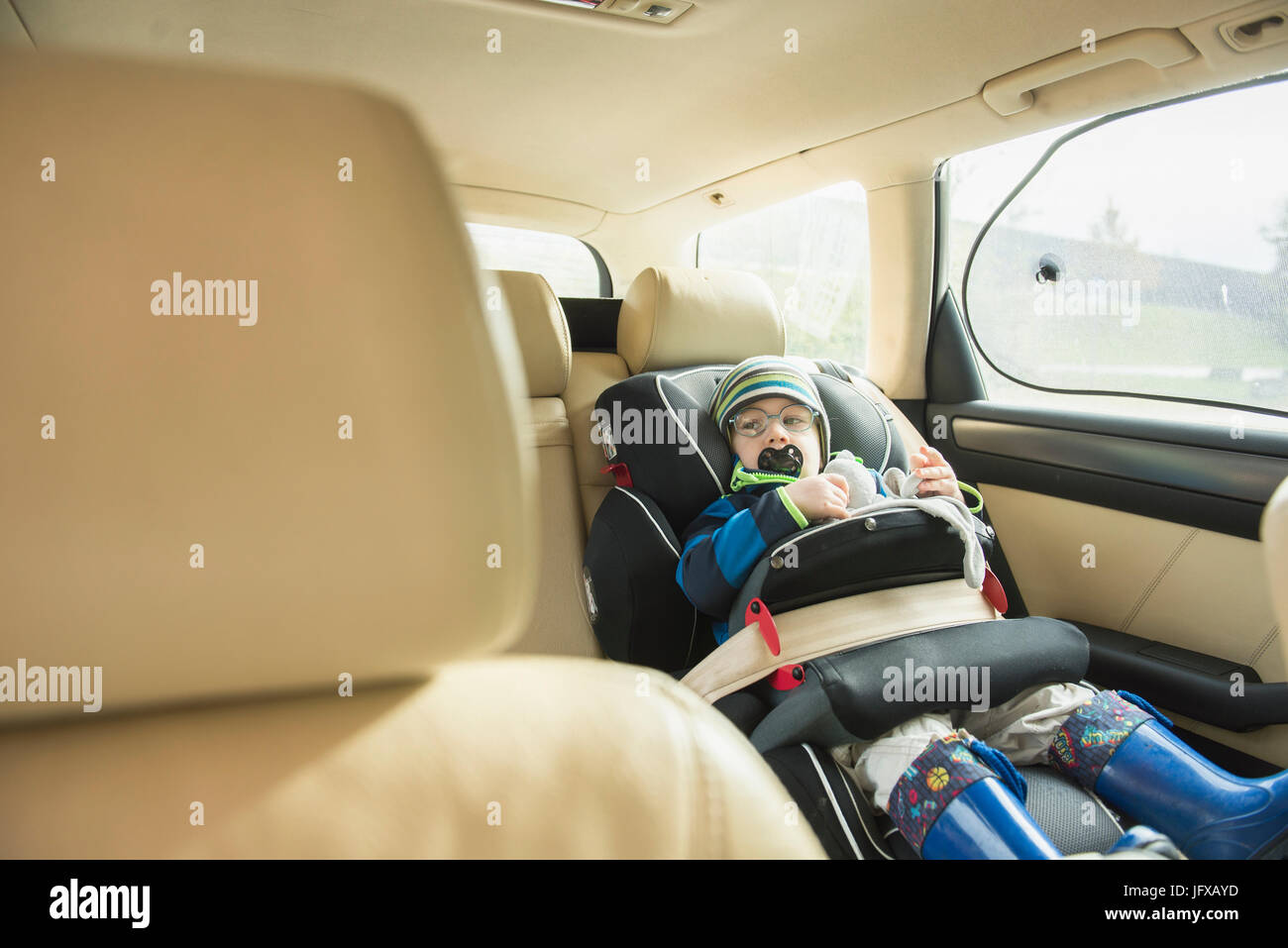 Kleiner Junge mit Schnuller im Mund sitzen im Autositz Stockfoto