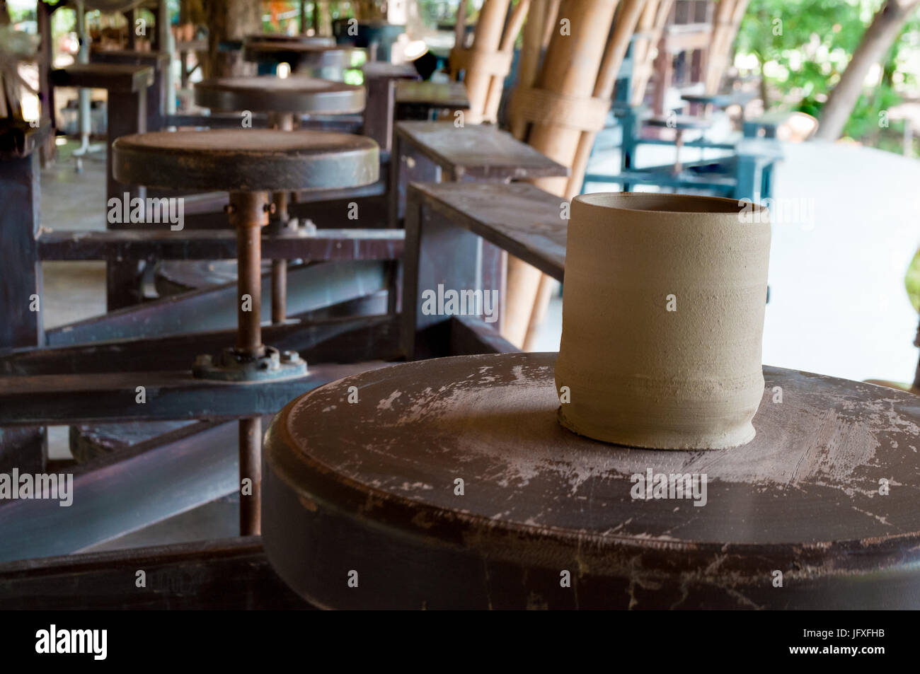 Getrocknete handgefertigten Tonwaren Ton Cup auf der Festplatte der kick Rad Workstation mit mehr leere Workstations im Hintergrund von Töpferei verwischt. Stockfoto