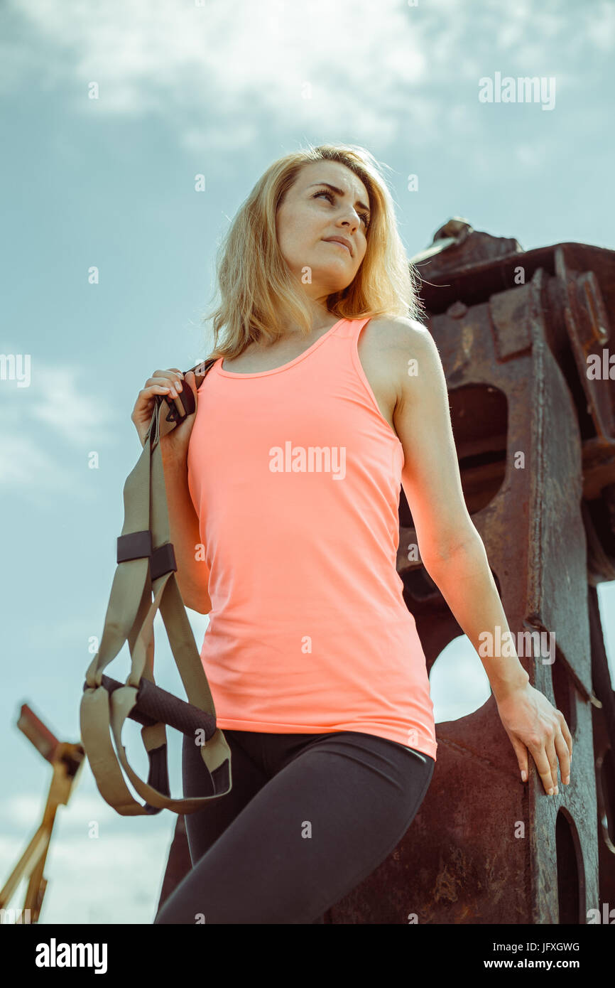 Blonde Fitness Frau posiert mit Trx Fitness Riemen auf rostigen Metalloberfläche Stockfoto