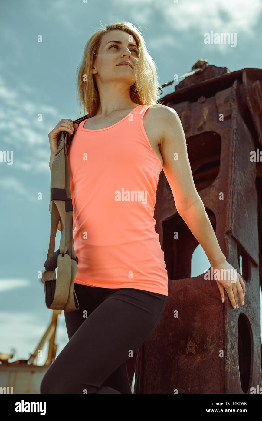 Blonde Fitness Frau posiert mit Trx Fitness Riemen auf rostigen Metalloberfläche Stockfoto