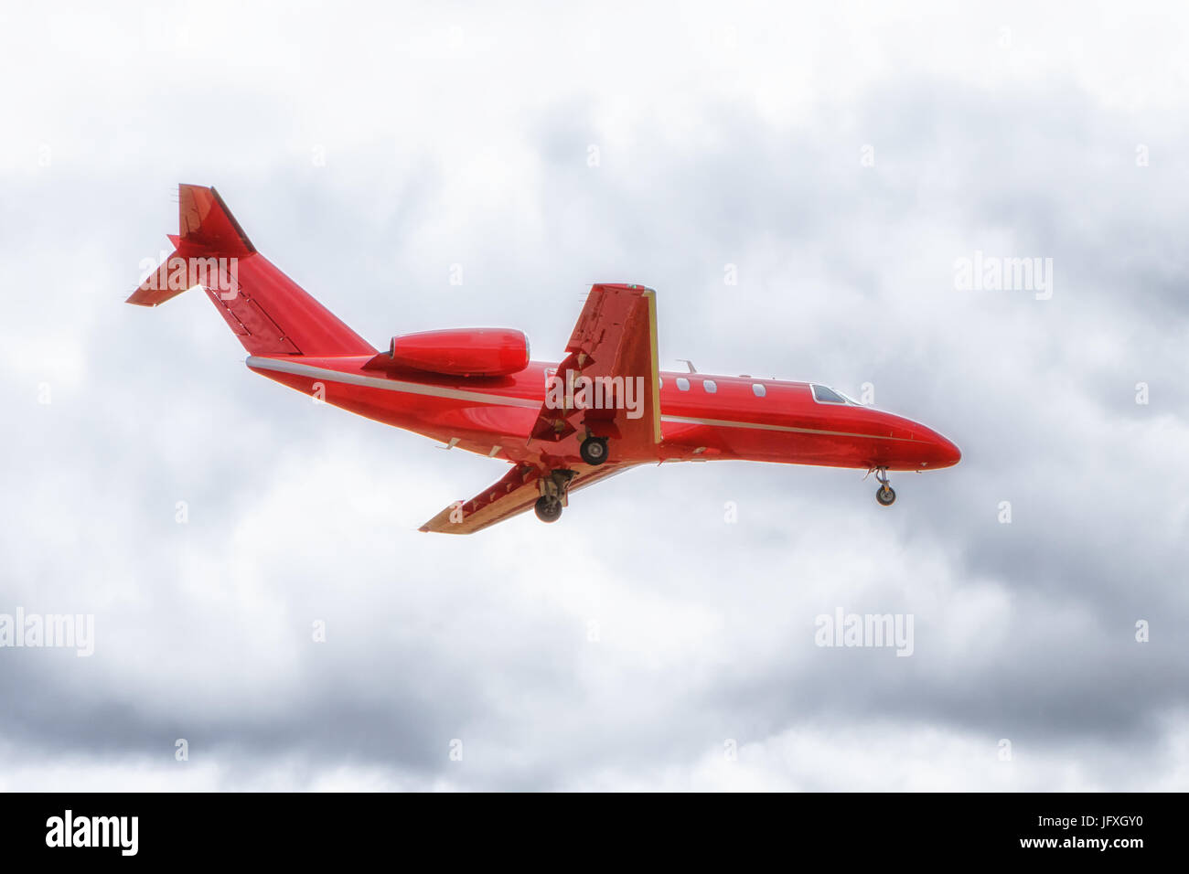 Ansicht von oben eine rote Business Jet Flugzeug kurz vor der Landung. bedeckt, bewölkten Himmel. Stockfoto