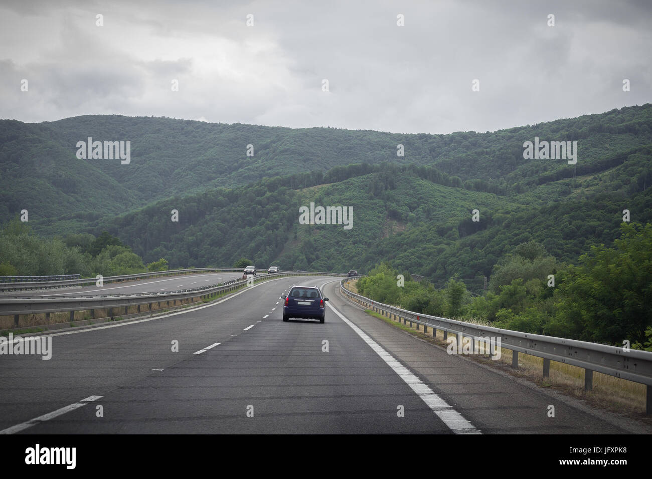 Asphaltierte Straße und Auto in den Bergen mit bewölktem Himmel im Hintergrund. Stockfoto