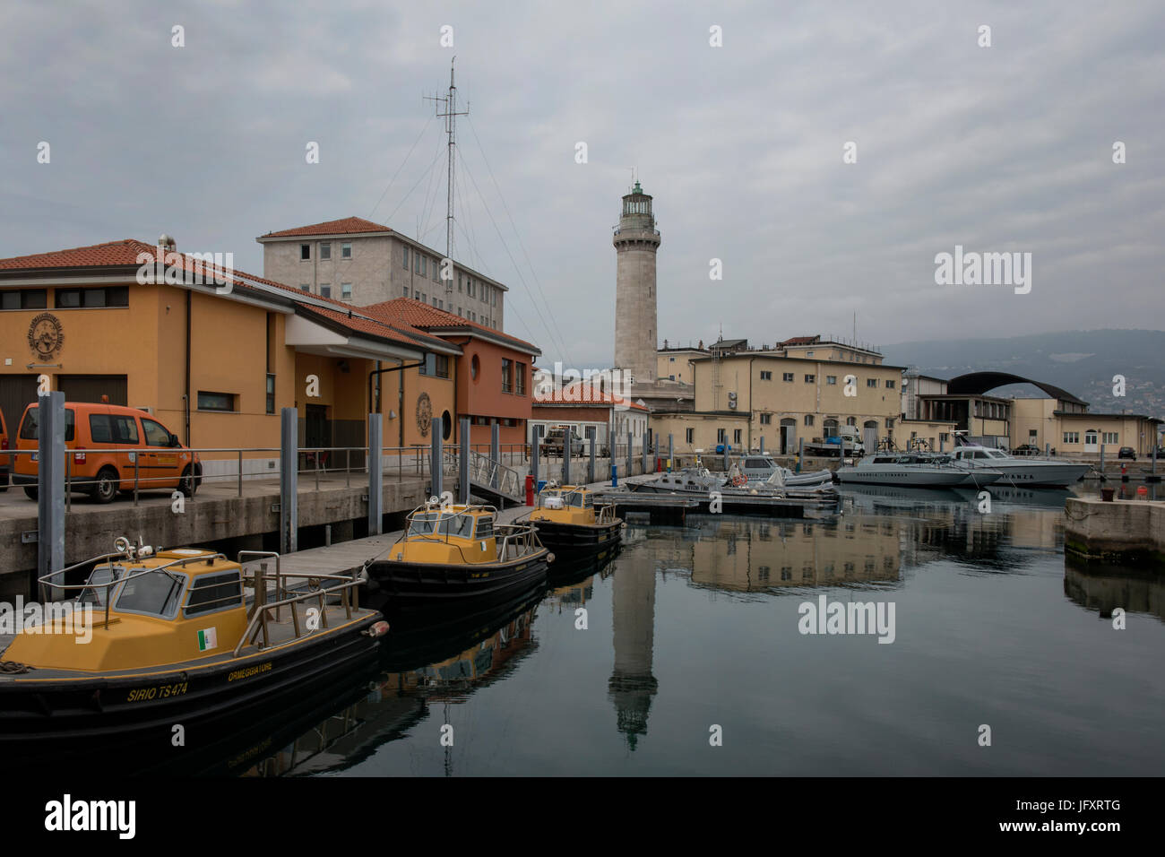 Schlepper und Patrouillenboote der Guardia di Finanza angedockt an der Mole "Fratelli Bandiera" mit dem alten Leuchtturm "Lanterna". Triest, Italien. Stockfoto