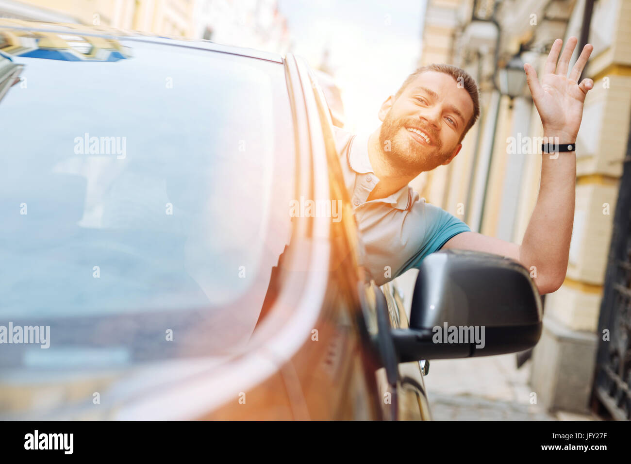 Charmanter Mann Hallo aus seinem Auto zu einem Passanten winken Stockfoto