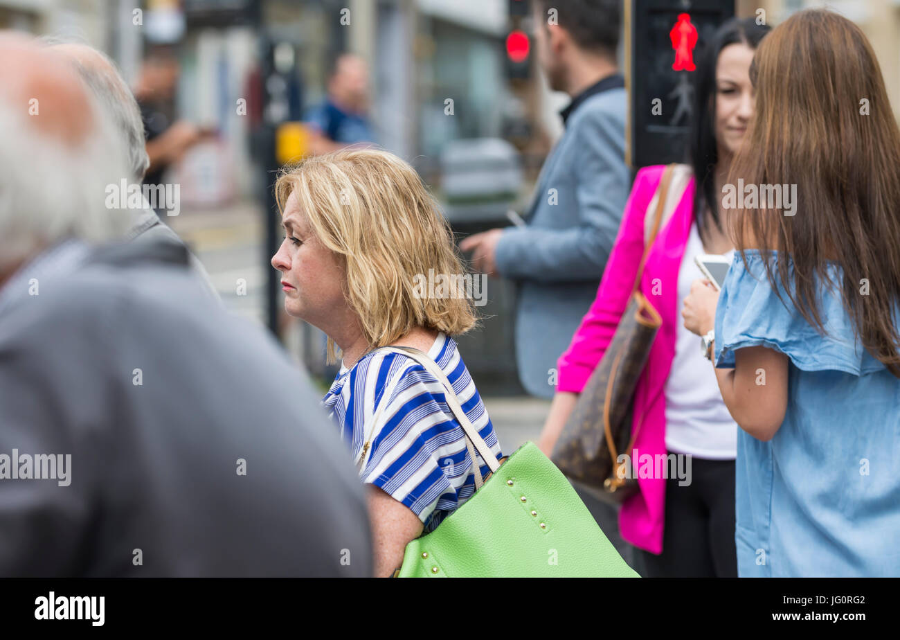 Menschen warten an der Ampel überqueren Sie eine Straße in einer geschäftigen Stadt in Großbritannien. Stockfoto