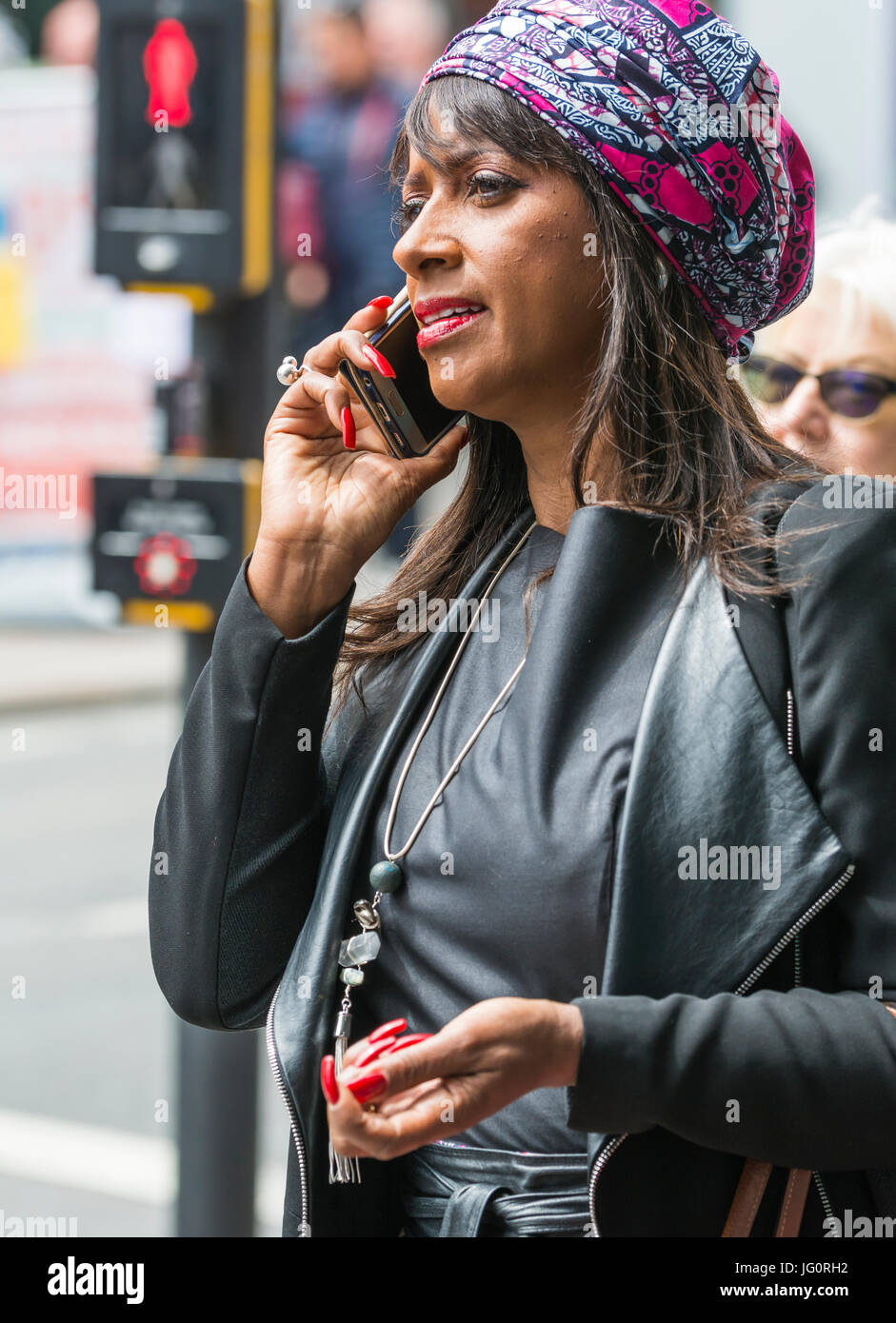 Frau von ethnischen Herkunft tragen intelligente Kleidung und ein Kopf Scrarf beim gehen in der Stadt und auf ihrem Handy zu sprechen. Stockfoto