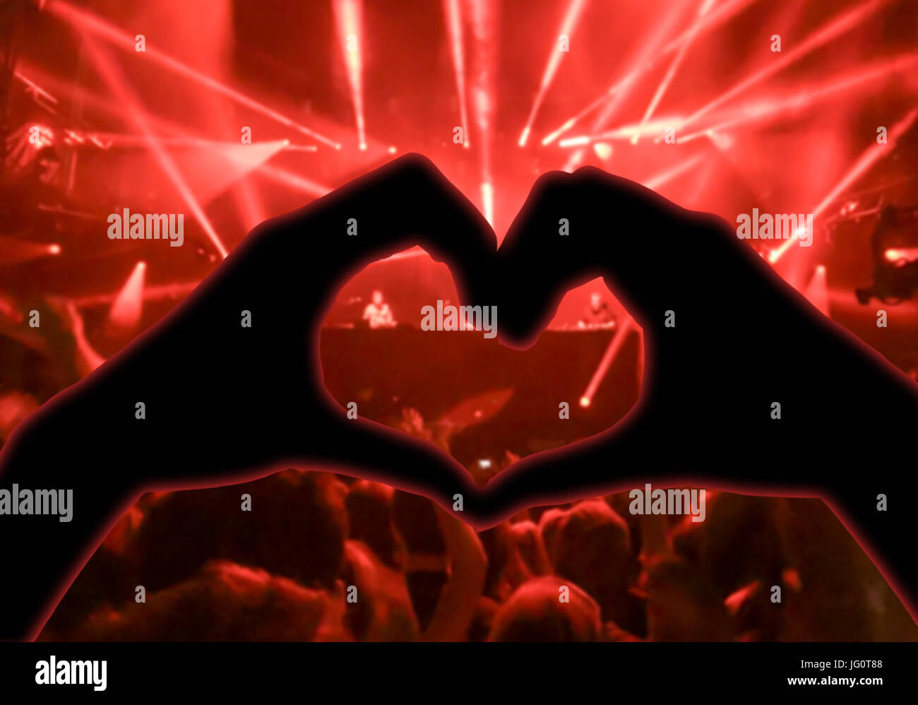 Konzert, Handzeichen in der Form des Herzens für die Musik, verschwommene Publikum und Künstler auf der Bühne im Hintergrund mit roten Strahlern Stockfoto