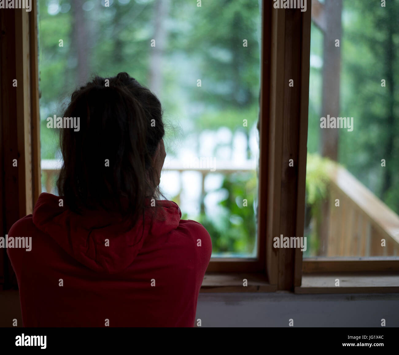 Junge braune behaarte weibliche Blick Fenster Haus am Wald an einem regnerischen Tag. Stockfoto