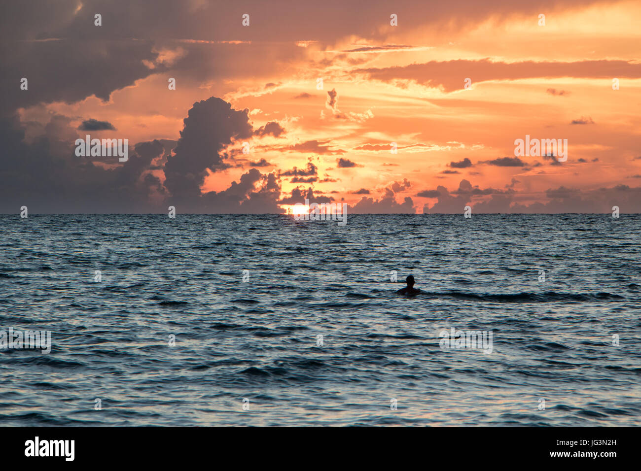 Mann im Ozean schwimmen bei Sonnenuntergang Stockfoto