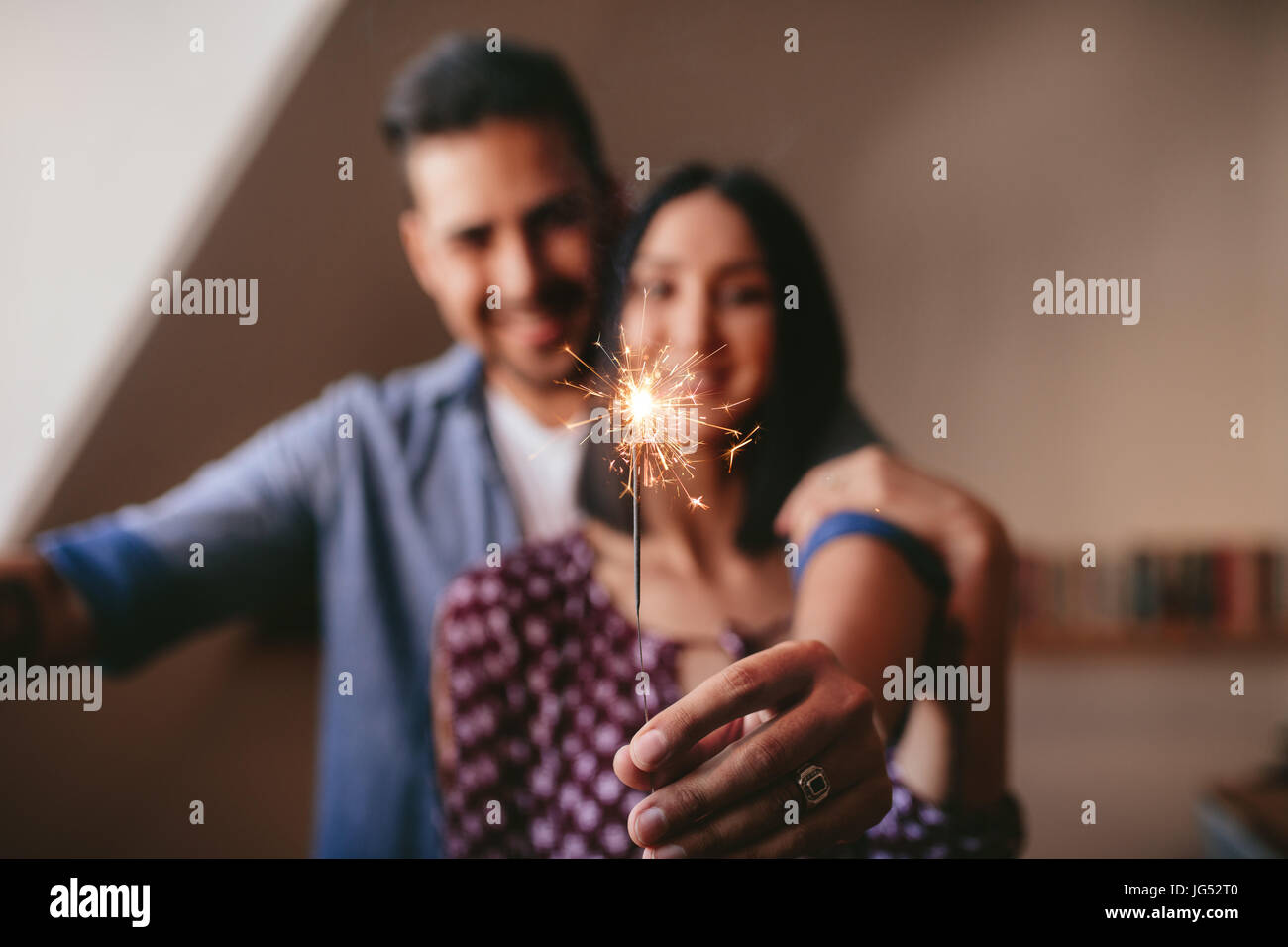 Junges Paar mit Wunderkerze drinnen feiern. Wunderkerze in der Hand des Menschen mit seiner Freundin zu Hause stehen. Stockfoto