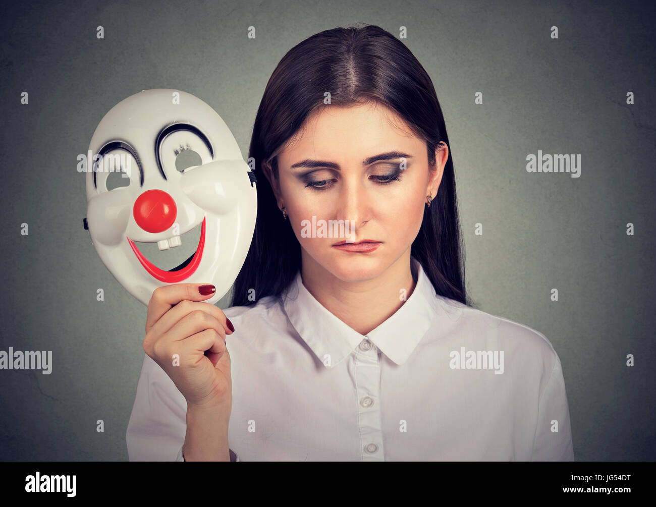 Porträt traurige Frau ausziehen Clownsmaske mit dem Ausdruck Glück auf graue Wand Hintergrund isoliert Stockfoto