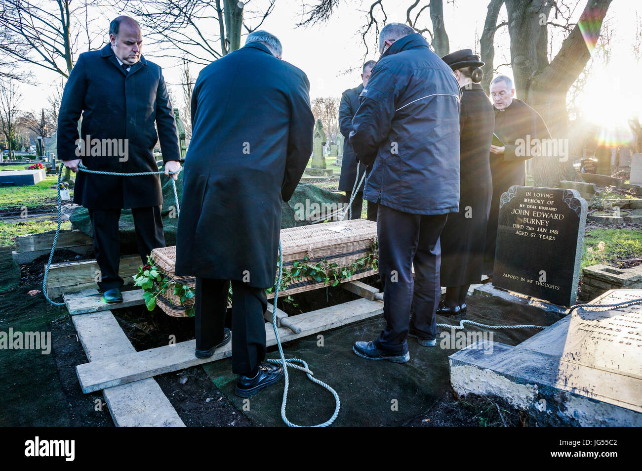 Eine Gruppe von Männern, die einen wicker Sarg mit Seilen, bereit, in ein Grab auf einem Friedhof in England, UK abgesenkt werden. Stockfoto