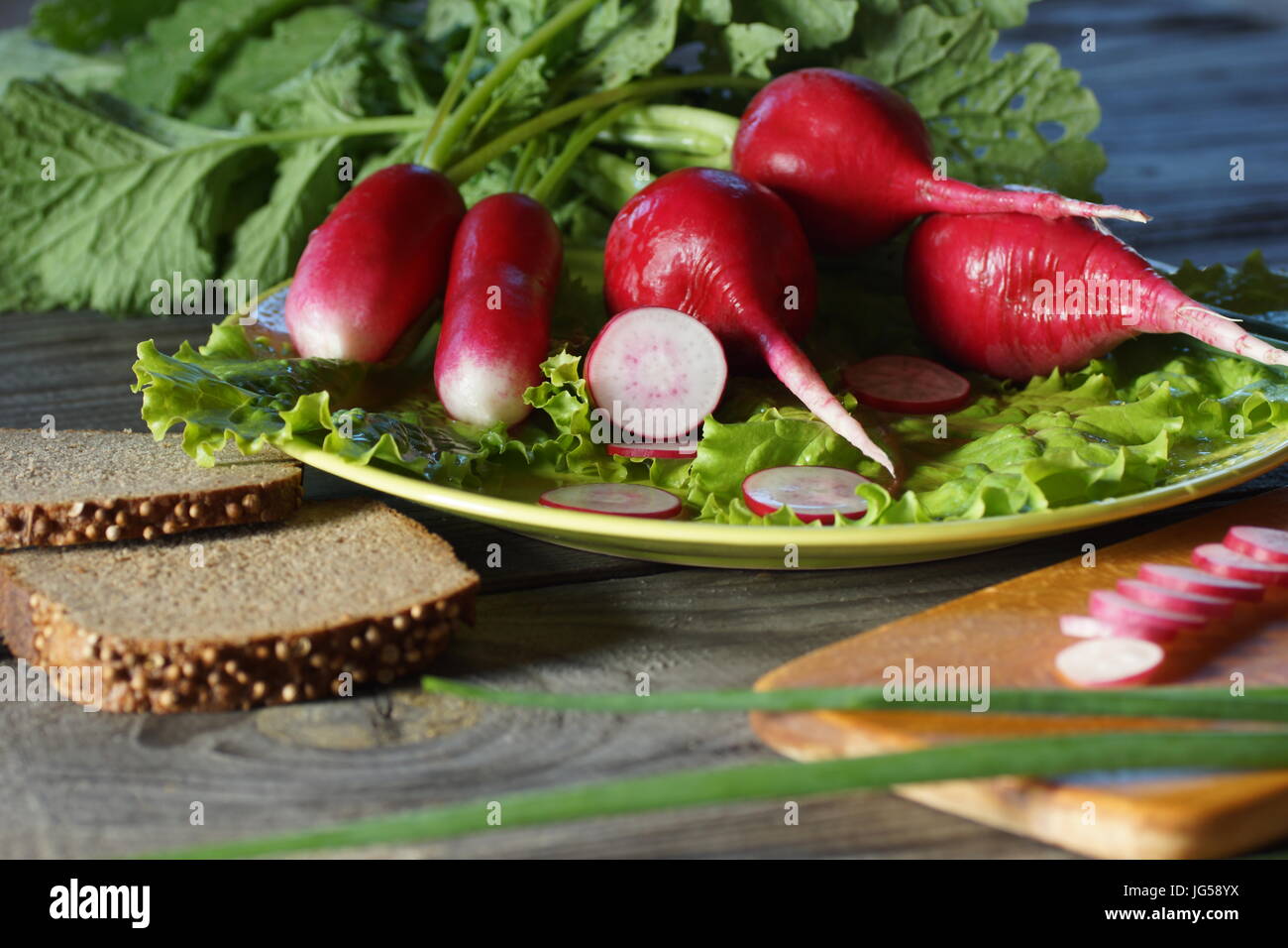 Stillleben mit Rettich, Salat, Frühlingszwiebeln und Brot. Radieschen und Salat Blätter liegen auf einem Teller. Saubere Radieschen vorbereitet wenden in die Nahrung. Stockfoto