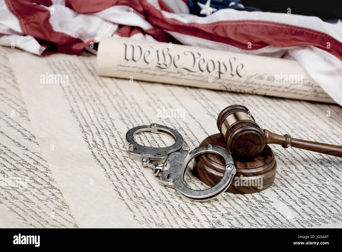 Verfassung der Vereinigten Staaten auf eine amerikanische Flagge mit einem Hammer und Handschellen im Vordergrund aufgerollt. Stockfoto