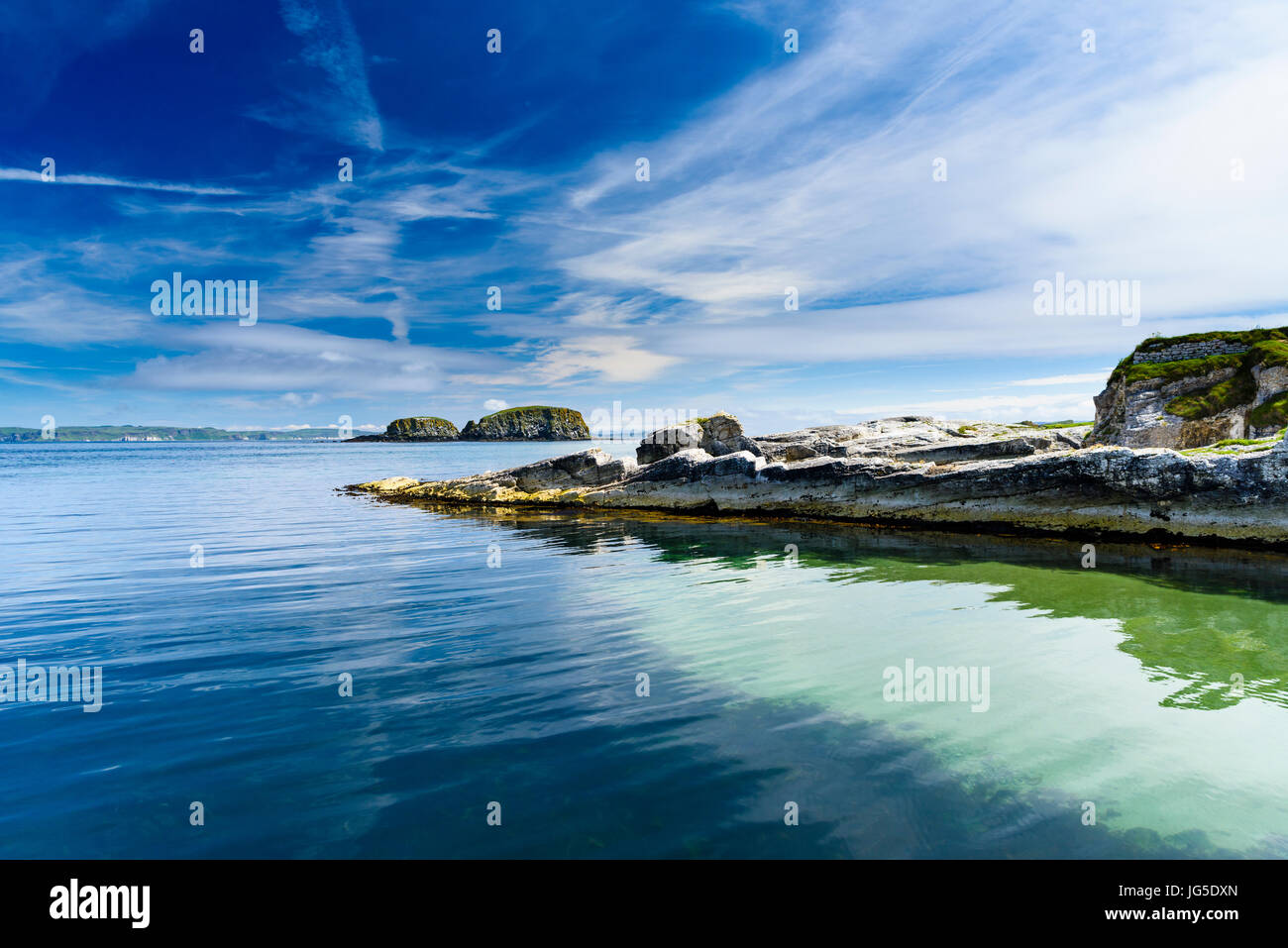 An der Küste Felsen mit einer sehr ruhigen Meer, blauer Himmel, Nordirland Stockfoto