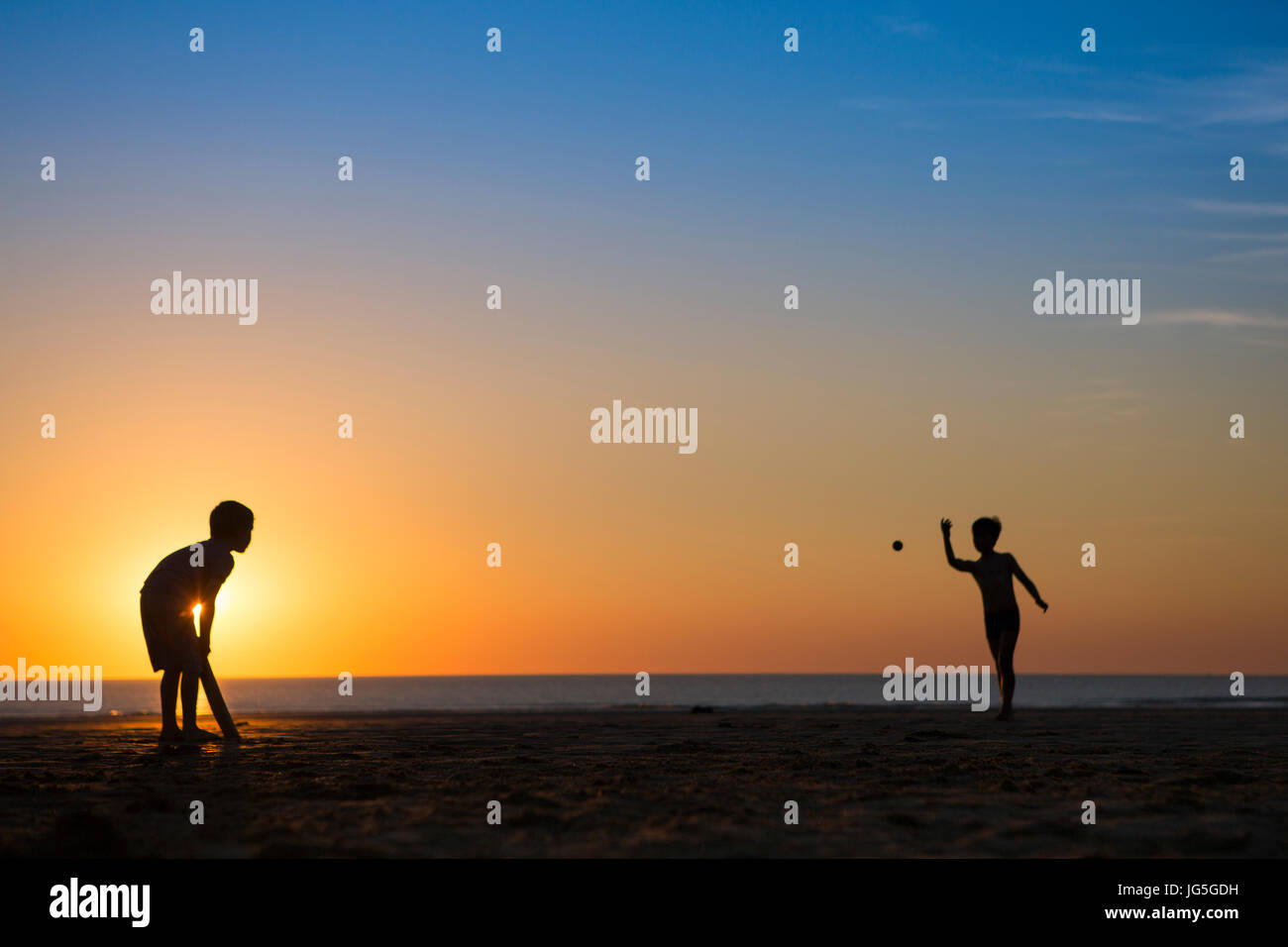 Zwei Jungen spielen Cricket am Strand, als die Sonne, Devon UK untergeht Stockfoto