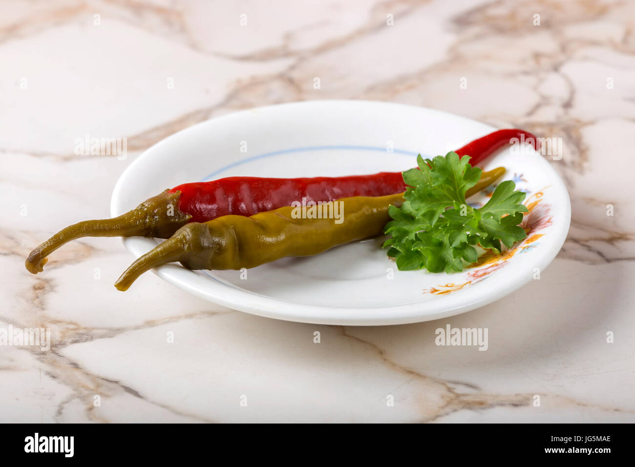 Eingelegte grüne und rote Peperoni Pfeffer in Teller auf den Tisch mit Petersilie Stockfoto