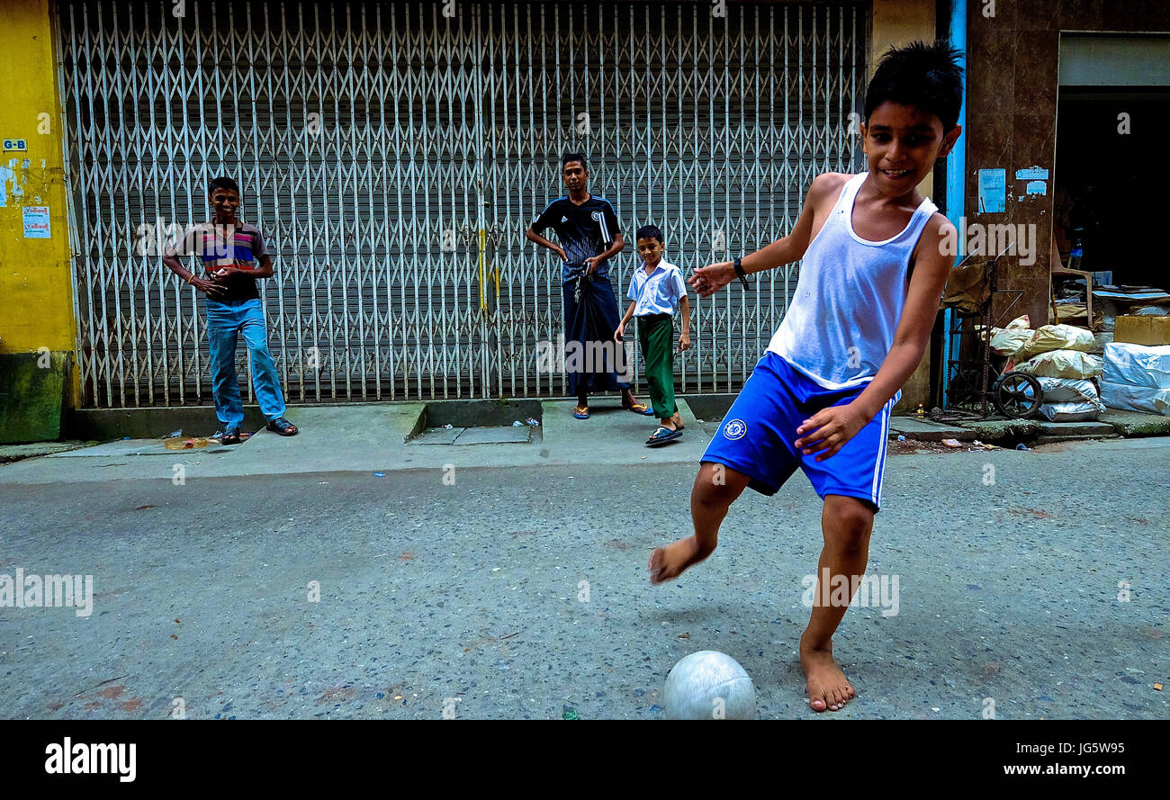 Ein Junge spielt Fußball auf der Straße in der Innenstadt von Yangon, Myanmar Stockfoto