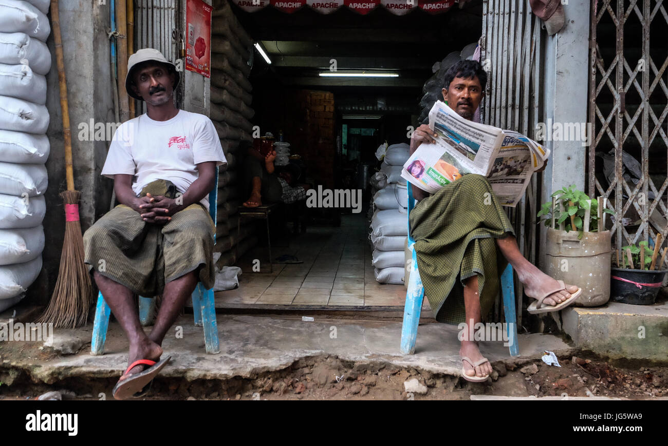 Arbeiter sitzen vor ihrem Geschäft in der Innenstadt von Yangon, Myanmar Stockfoto