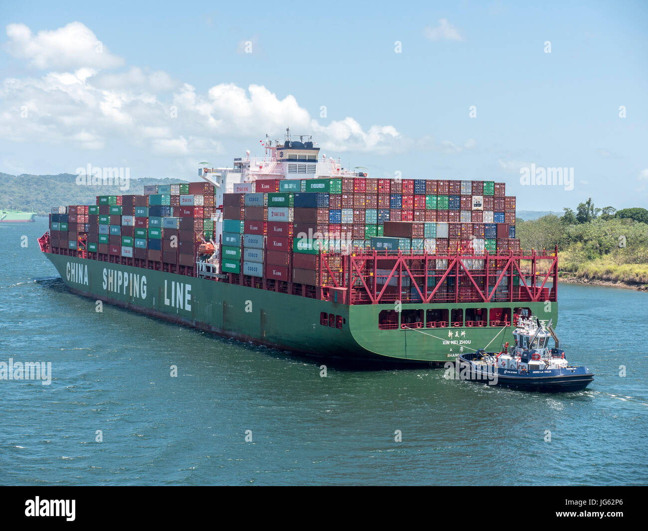 Ein Containerschiff Xin Mei Zhou der China Reederei auf der Durchreise Gatun See des Panama-Kanals, gesteuert von einem Schlepper Stockfoto