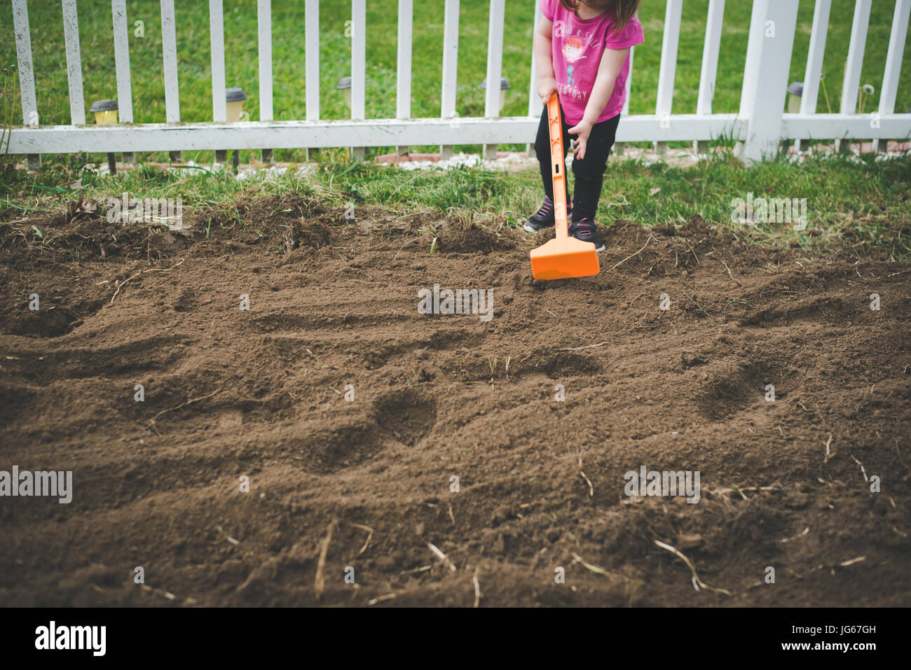 Ein Kleinkind hilft, ein Garten in einem Hinterhof zu Hacke. Stockfoto