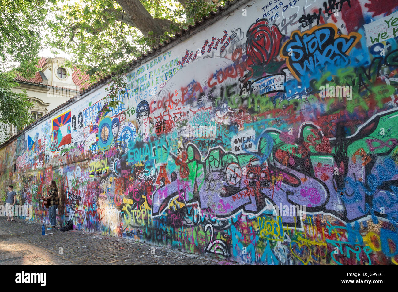 Ein Tourist und Straßenmusiker an der John-Lennon-Mauer in Prag. Es ist eine Wand mit Stücken von songtexte von Beatles Songs und John Lennon inspirierten Graffiti. Stockfoto