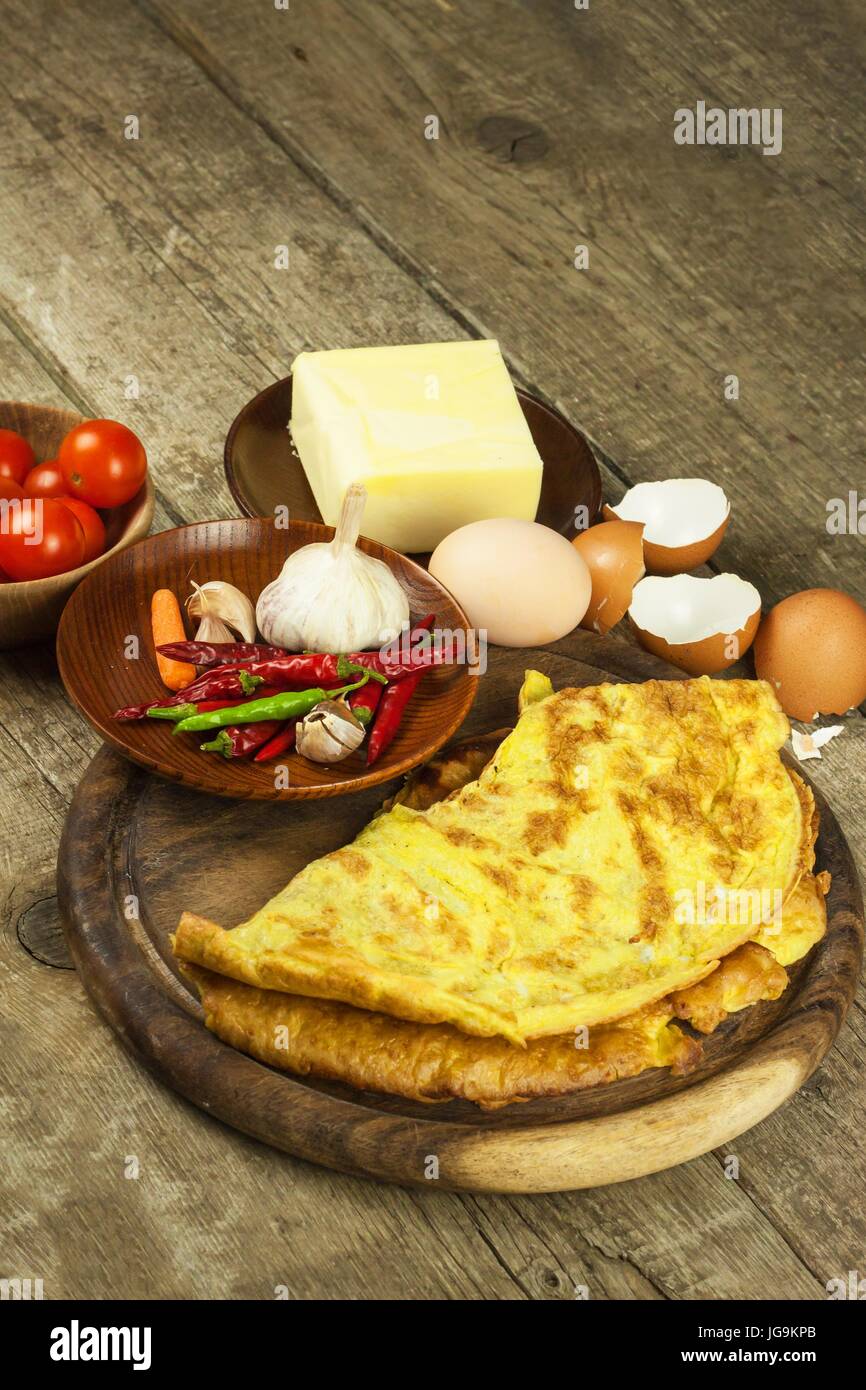 Lecker gefüllte Omelette auf einem Holzbrett. Gebratenes Ei Omelett mit Cherry-Tomaten, Knoblauch und Chili Peppers. Nahrhaftes Frühstück Stockfoto