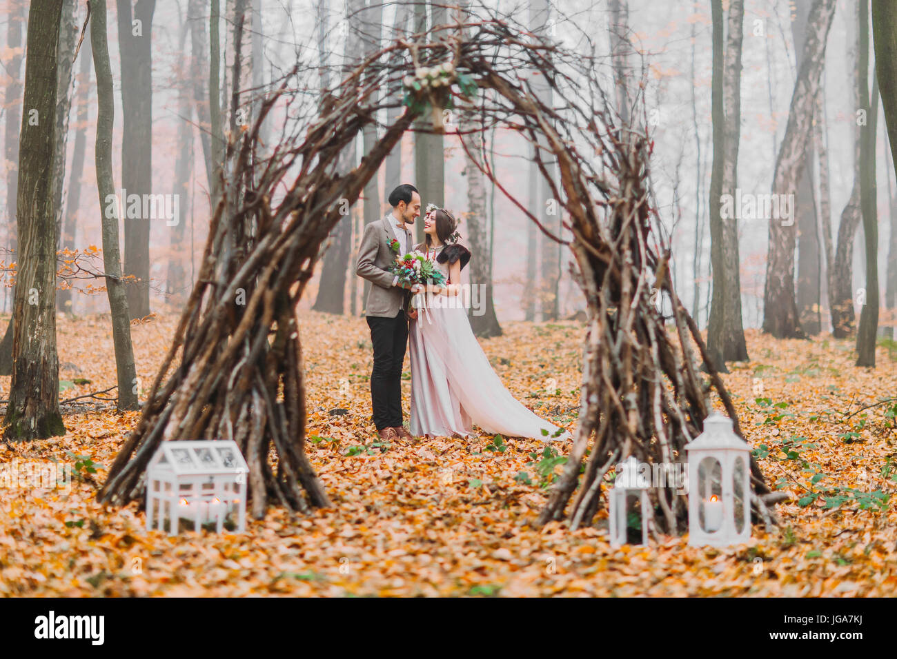 Glücklich Brünette Brautpaar schauen liebevoll einander unter dem kreativen hübsch dekorierte Hochzeit Bogen im herbstlichen Wald Stockfoto