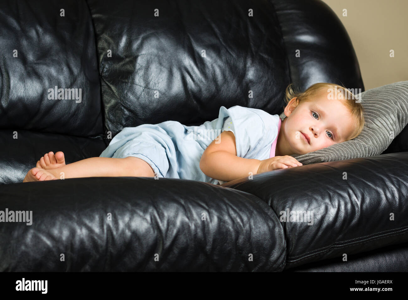 2 Jahre altes Mädchen im blauen Pyjama liegen auf der Couch Tagträumen Stockfoto
