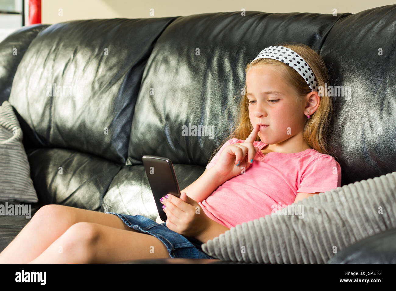 Hübsches kleines Mädchen mit Smartphone auf der couch Stockfoto