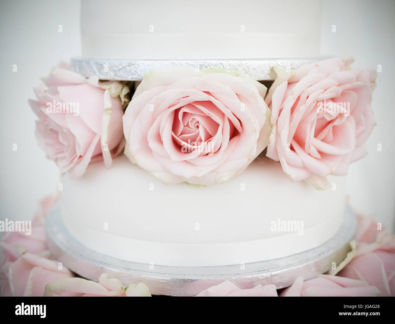 Eine Nahaufnahme von einer Hochzeitstorte mit rosa Rosen und weißen Zuckerguss in Pastellfarben Stockfoto