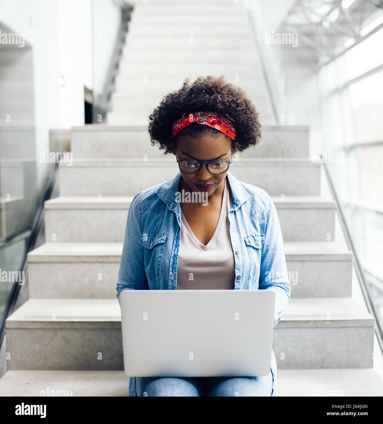 Fokussierte junge afrikanische Unternehmerin sitzen in einem Treppenhaus eines modernen Bürogebäudes hart bei der Arbeit auf einem laptop Stockfoto