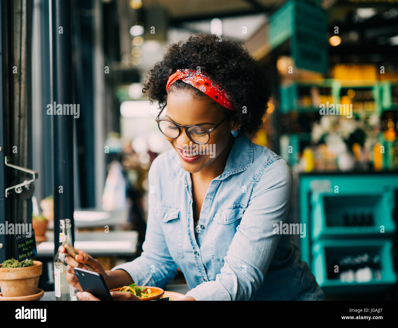 Lächelnde junge Afrikanerin Lesetexte auf ein Handy beim Sitzen allein an einem Schalter in einem Café genießen Sie eine Mahlzeit Stockfoto