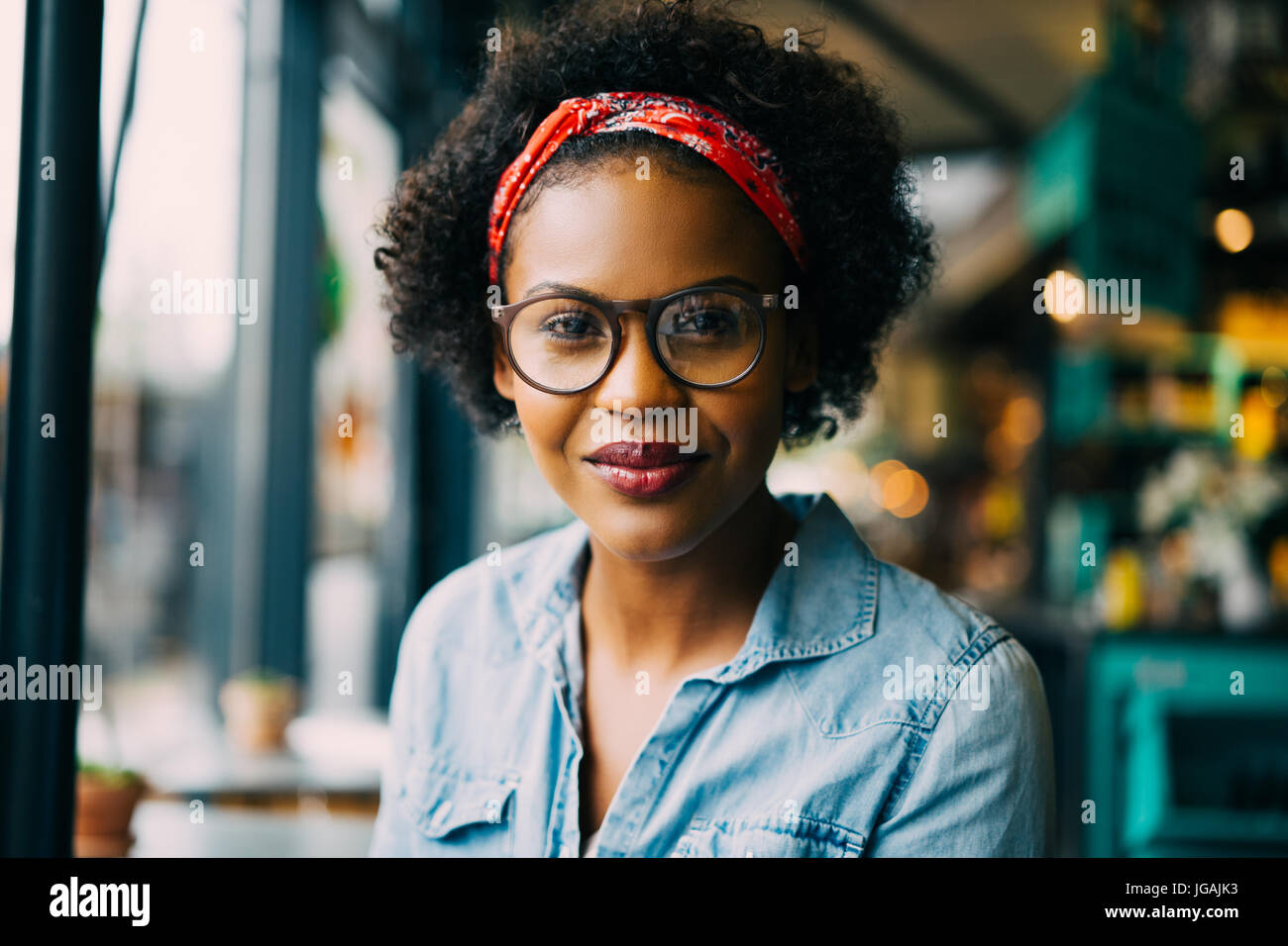 Porträt von einer attraktiven jungen Afrikanerin Brillen-und ein Halstuch zufrieden lächelnd, während Sie sitzen allein in einem café Stockfoto
