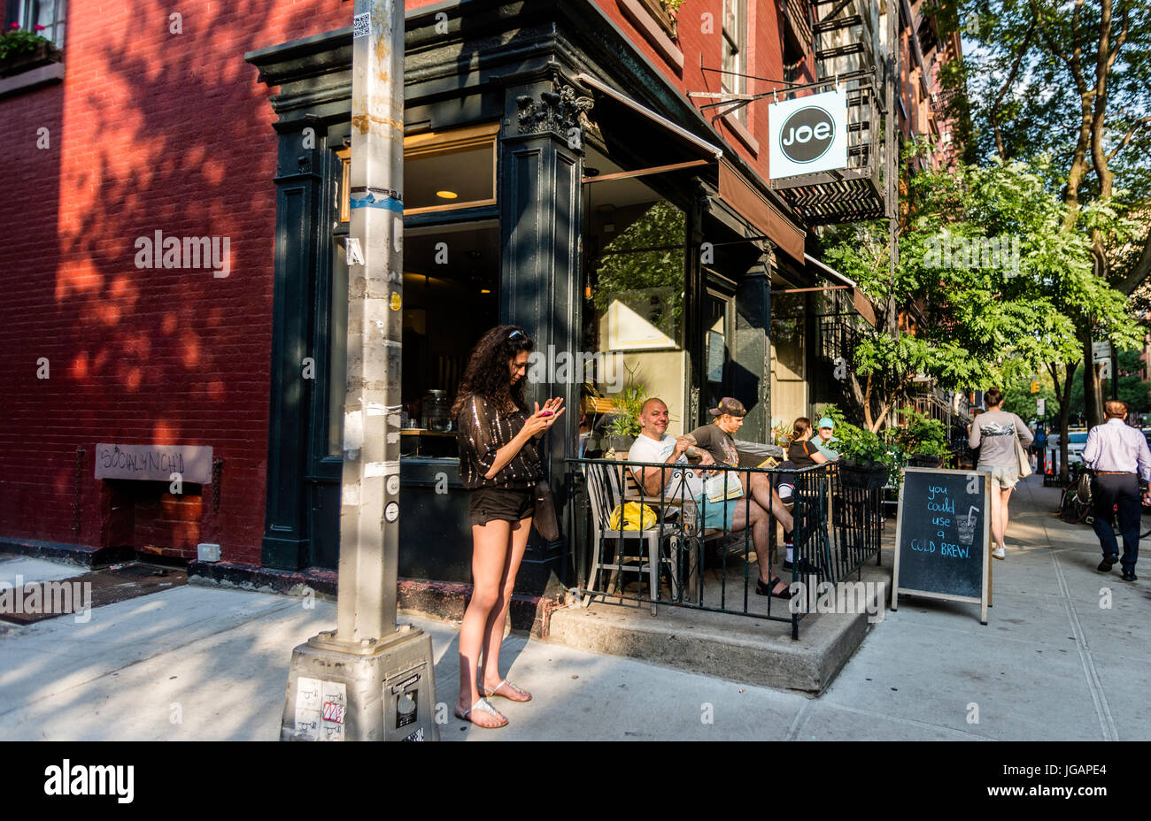 New York, NY, USA, eine Frau in Sandalen und Shorts Texte auf einem Smartphone außerhalb Joe, ein Café am Waverly Place in Greenwich Village. © Stacy Walsh Rosenstock Stockfoto