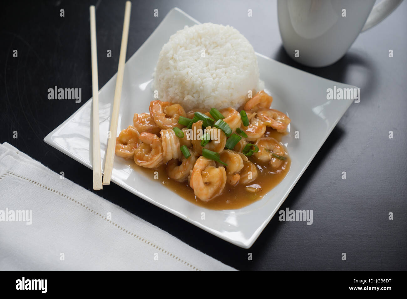 Szechuan Garnelen und Reis mit Frühlingszwiebeln auf weißen Teller mit Stäbchen. Stockfoto