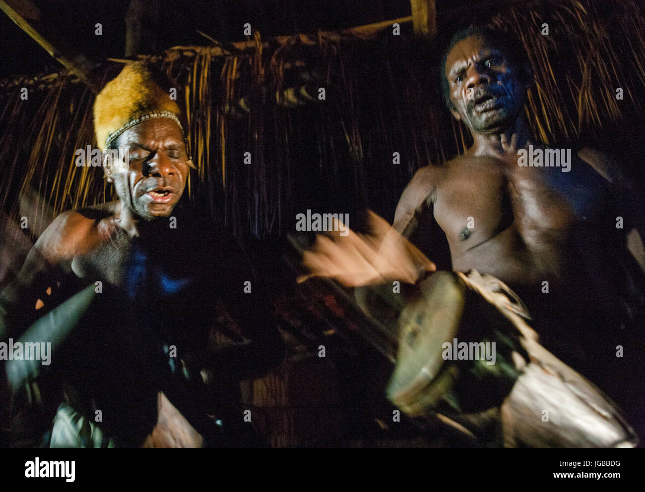 Indonesien, IRIAN JAYA, ASMAT Provinz, JOW Dorf - Juni 12: Männer Asmat Stamm sitzen zu Hause und auf der Trommel zu spielen. Stockfoto
