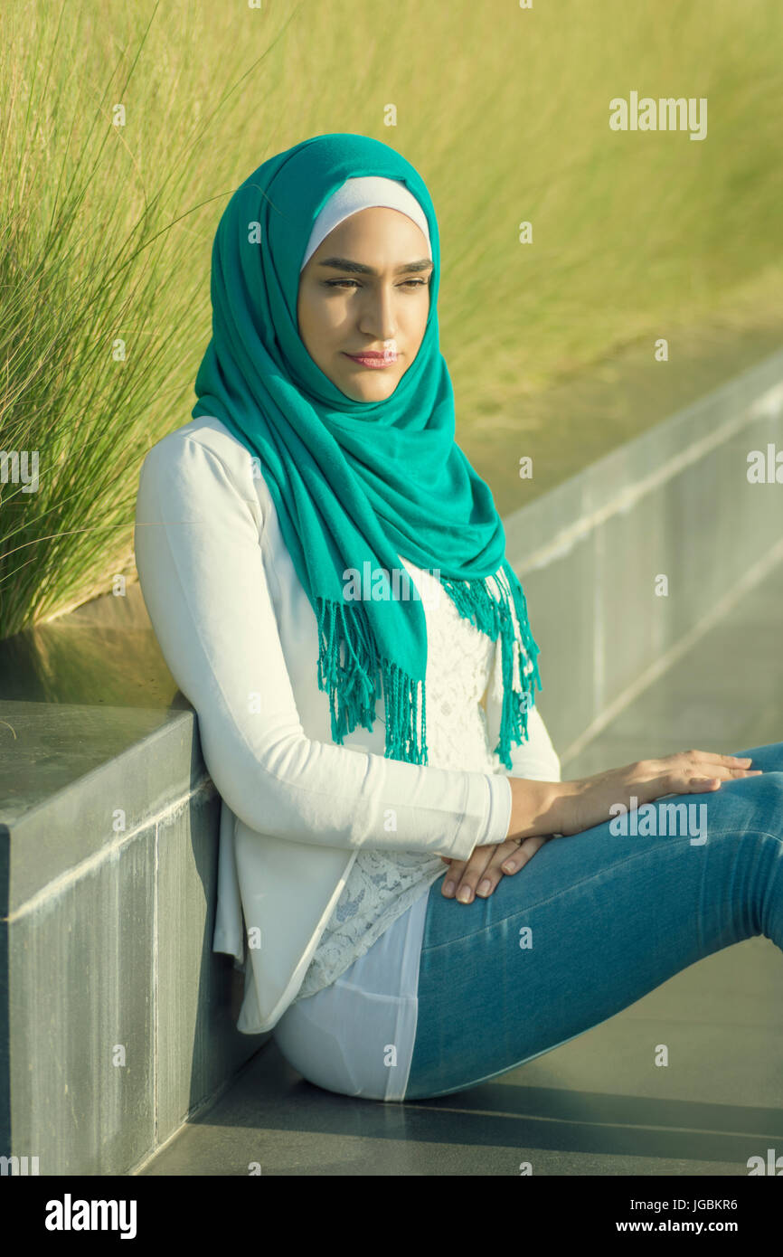 Ernste junge muslimische Frau tragen Hijab sitzen im freien wegschauen Stockfoto