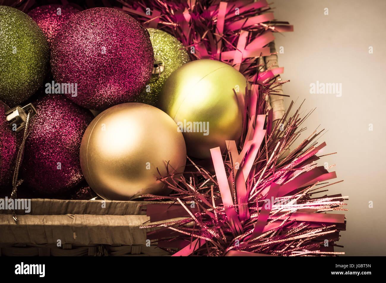 Weihnachtskugeln in rosa, grüne und goldene Farbtönen mit Lametta in einem geöffneten Korb zu bedeuten Auspacken aus dem Speicher in Vorbereitung auf die Ferien Kranz Stockfoto